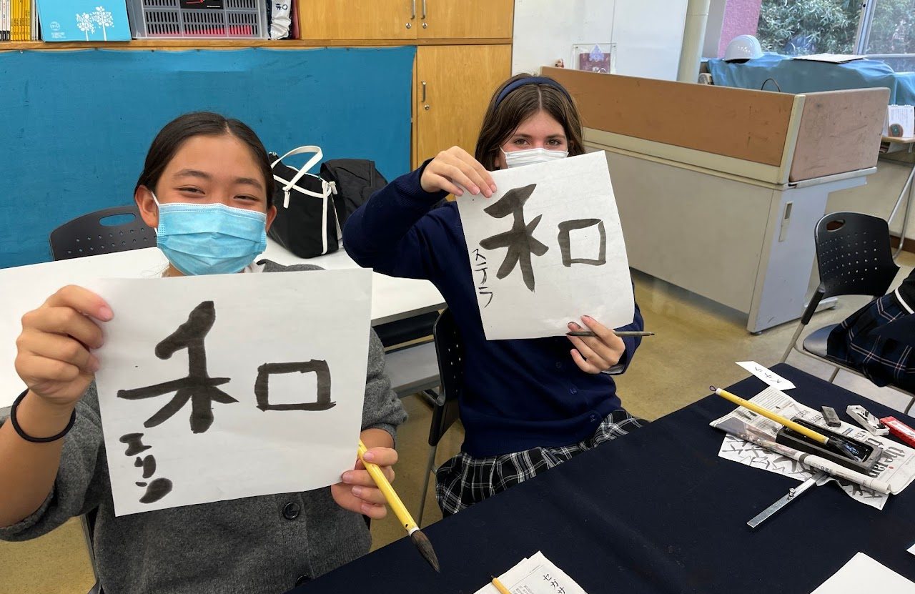 Stella and a classmate holding calligraphy of the kanji 和, harmony